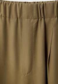 Gros plan sur un pantalon kaki à taille élastique avec des coutures visibles et une ouverture de poche latérale.