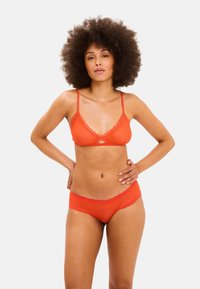Bralette dengan trim renda merah yang memiliki tali yang dapat disesuaikan, dipasangkan dengan celana dalam aksen renda yang sesuai. Kain halus, desain sederhana dan warna cerah.