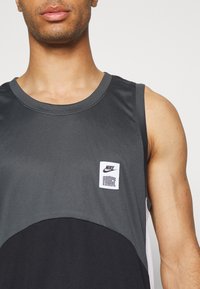 Sivi i crni bez rukava Nike majica sa okruglim izrezom i teksturiranom tkaninom, s vidljivom bijelom oznakom.
