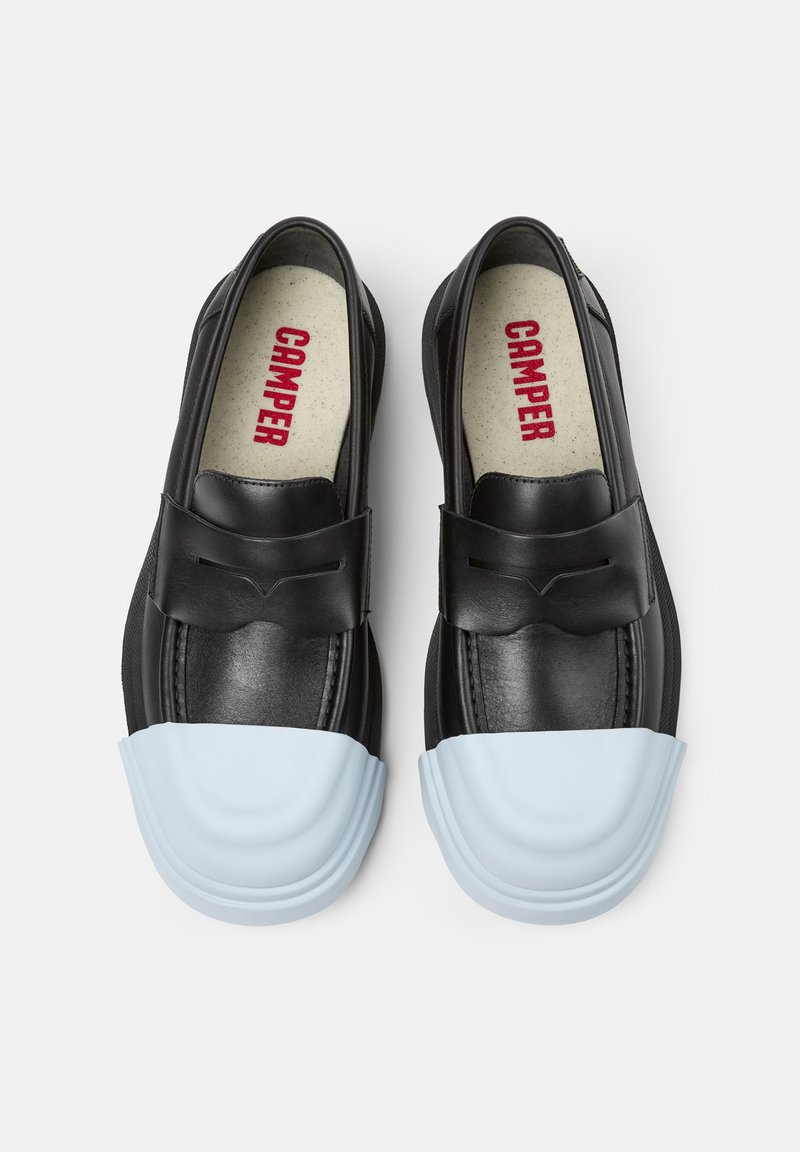 Scarpe slip-on nere in pelle con punta in gomma blu. Presentano un design elegante e un sottile dettaglio a fiocco sulla parte anteriore.