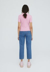 Top rosa a maniche corte a coste abbinato a jeans blu a vita alta e gamba dritta, con scarpe da ginnastica piattaforme rosa chiaro. Vista dal retro.