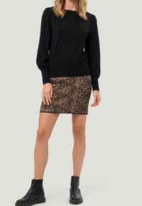 Pull en tricot noir avec des manches volantes, associé à une jupe courte à motif texturé brun et noir. Bottines noires.