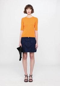 Kratka rebrasta oranžna pulover s kratkimi rokavi, v kombinaciji s temno modrim denim krilom s žepi, dodatno pa s črno torbico.