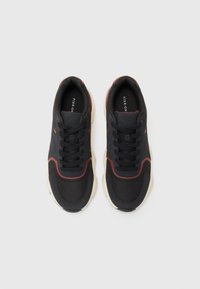 Black sporty sneakers with red accents, textured fabric, rounded toe, chunky sole, and black laces, featuring branding inside the tongue.