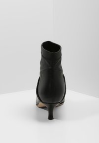 Bottines noires avec une finition en cuir lisse, un talon effilé et un design sans couture. L'intérieur est doublé, avec une silhouette basse.