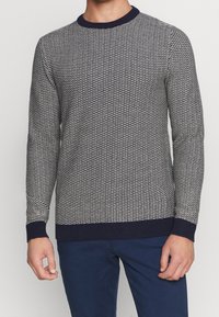 Modrý a bílý svetr se vzorem, kulatým výstřihem, žebernými manžetami a lemem. Vyroben z texturované pleteniny.