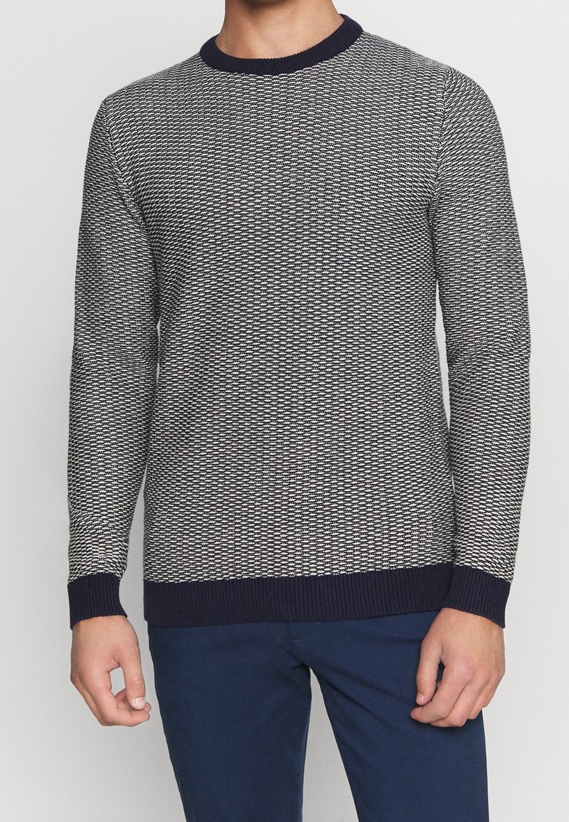 Modrý a bílý svetr se vzorem, kulatým výstřihem, žebernými manžetami a lemem. Vyroben z texturované pleteniny.