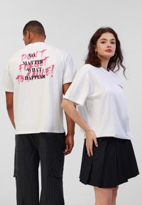 Hvite bomulls t-skjorter med fet rosa og svart tekst på ryggen. Modellen kombinerer med sort pinstripe skjørt og bukser med cargo-lommer.