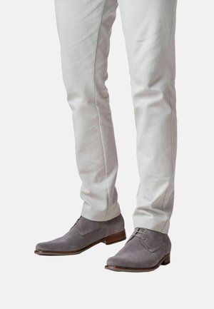 Grijze, gestructureerde nette schoenen met een gladde bruine zool en een afgeronde neus, gecombineerd met lichtgekleurde, nauwsluitende broek die een nauwsluitende pasvorm toont.