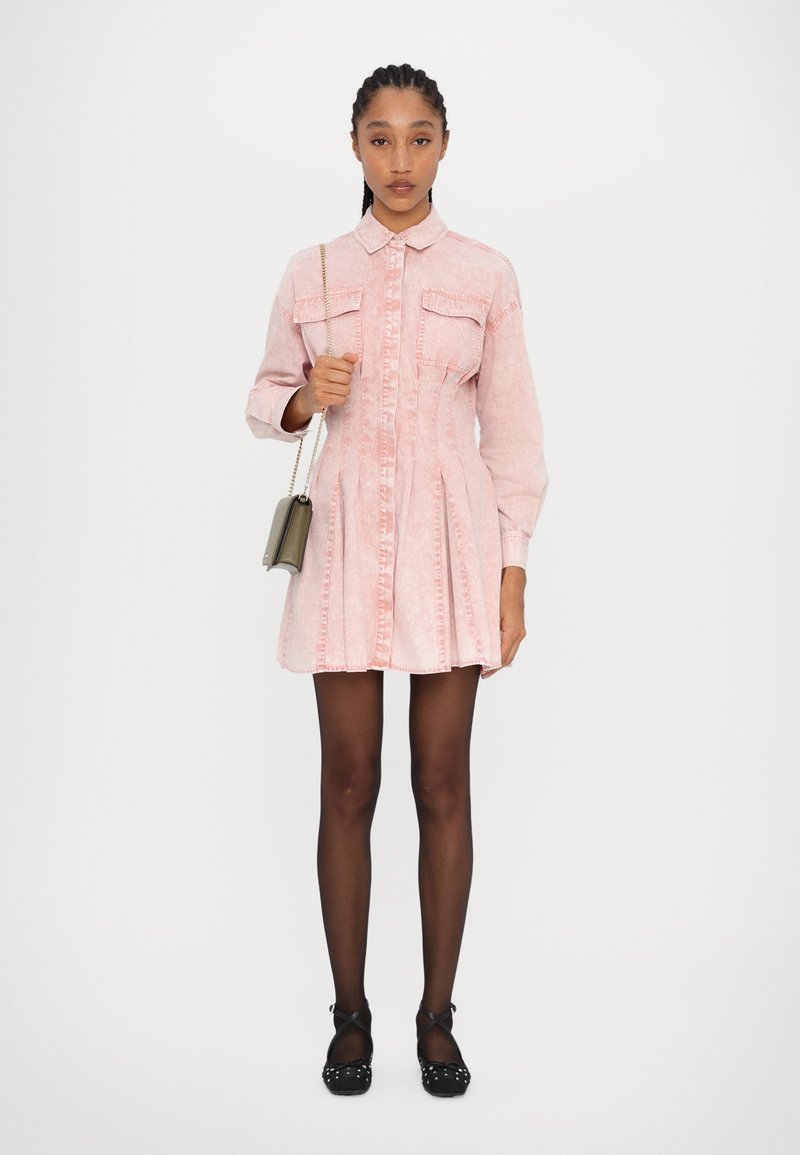 Rosa denimkjole med krage, knappestengt front, to brystlommer og en utsvingt skjørt. Kombinert med svarte ballerinasko med prikkemønster og strømpebukse.