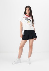 White cotton t-shirt with red neckline and Rolling Stones graphic, paired with a black pleated skirt and white high-top sneakers.