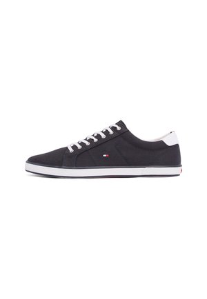 Schwarzer Sneaker mit niedrigem Schaft, weißen Schnürsenkeln und Sohle, kleinem rot-weiß-blauem Logo an der Seite und weißer Fersenlasche.