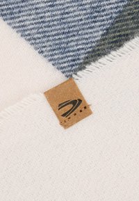 Wollmischung-Decke mit einem dreieckigen Design in Blau, Grün und Weiß, fransigen Kanten und einem braunen Lederschild mit Logo.