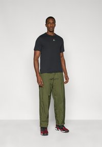 Μαύρο κοντομάνικο μπλουζάκι με μικρό λογότυπο, σε συνδυασμό με παντελόνι ελιάς και αθλητικά παπούτσια με κόκκινες λεπτομέρειες.