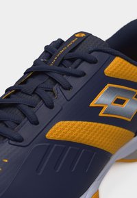 Αθλητικό παπούτσι σε ναυτικό μπλε και κίτρινο χρώμα με κορδόνια, υφασμάτινο διχτυωτό υλικό και ασημί λογότυπο στο πλάι, που εμφανίζει τις λεπτομέρειες του πάνω μέρους, μπροστά και στο πλάι.