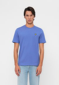 T-shirt en coton bleu à manches courtes et col rond. Présente un petit logo de papillon jaune sur la poitrine gauche. Coupe décontractée.