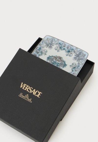Μαύρο κουτί Versace μερικώς ανοιχτό, που αποκαλύπτει ένα διακοσμητικό τετράγωνο πιάτο με περίτεχνα μπλε και γκρι ανθικά μπαρόκ σχέδια.