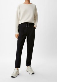 Light beige sweatshirt with a round neck, worn with black pants featuring a drawstring waist and side pockets, paired with white sneakers.