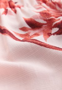 Tissu rose clair doux avec un motif floral rouge flou et une texture tissée visible, présenté en gros plan avec de légers plis.