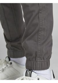 Grå avsmalnande byxor med elastiska muddar, tillverkade av mjukt tyg. Bärs med vita sneakers och vita strumpor med svart och vit accent.