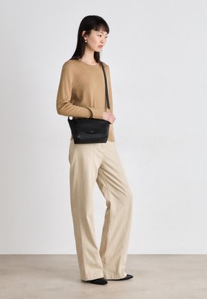 Borsa a tracolla in pelle nera con chiusura a zip, manico corto e discreto logo dorato, abbinata a un maglione sabbia e pantaloni beige a gamba larga.