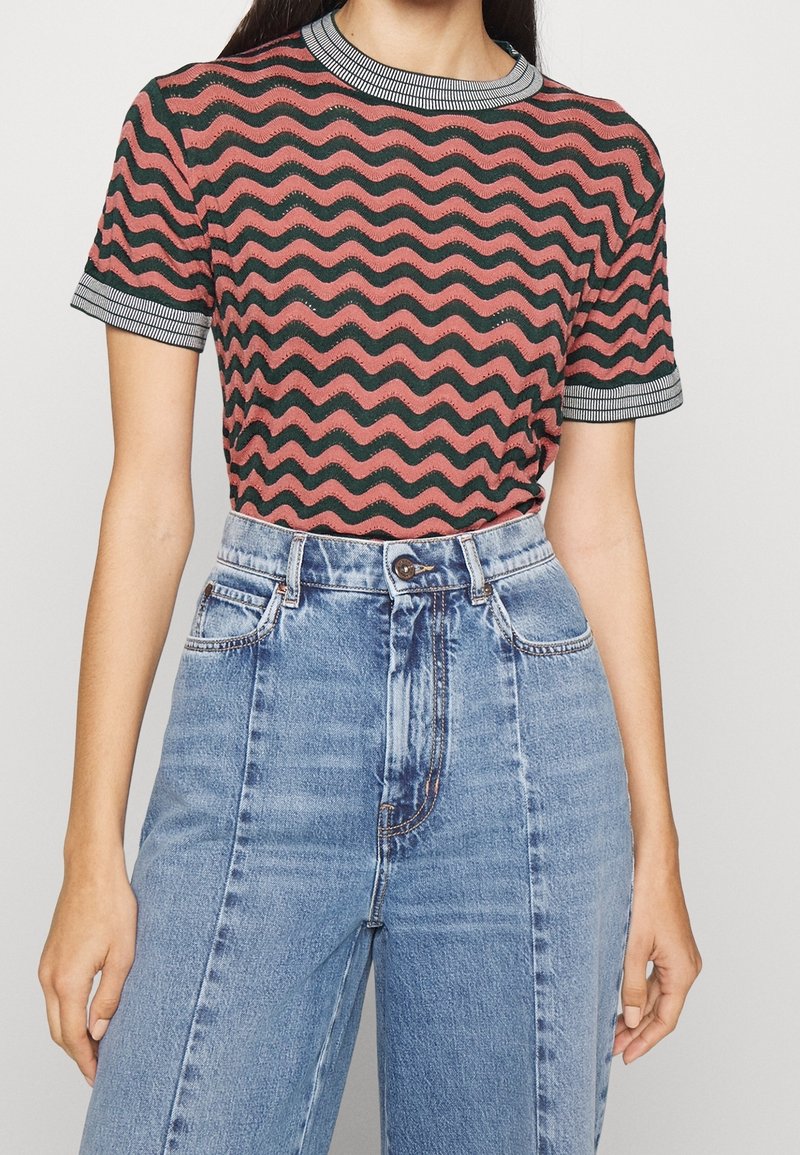 Rød og sort bølget mønstrede strikbluse med ribbet rund hals og korte ærmer, parret med højtaljede lyseblå jeans.