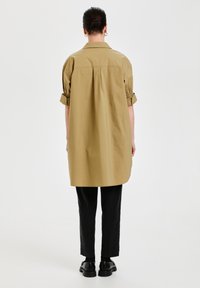 Vestito camicia khaki con un fit rilassato, maniche arrotolate e dettaglio a piega sul retro. Abbinato a pantaloni neri a sigaretta e scarpe nere chunky.