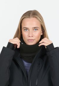 Svart halsvärmare i slät tyg, dragen under en svart jacka med dragkedja. Halsvärmaren är figurnära, utformad för värme och komfort.