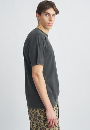 Czarny bawełniany t-shirt z krótkimi rękawami, okrągłym dekoltem i wyblakłą fakturą, zestawiony z beżowymi spodniami w panterkę z ciemnymi akcentami.