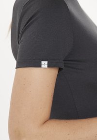 Donkergrijze T-shirt met korte mouwen, voorzien van een klein wit label met een hartslagontwerp op de mouw. Zachte, gladde stof met een aansluitende pasvorm.