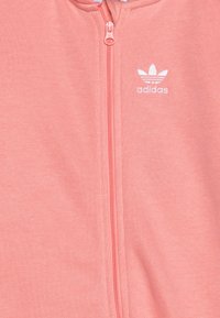 Roza zip-up dukserica iz mehkega blaga, z belim logotipom Adidas in gladkim sprednjim zadrgo. Preprost dizajn brez dodatnih vzorcev.