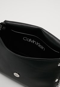 Sort læderhåndtaske med en glat tekstur, med sølvfarvet tryklås og indvendig label med teksten "Calvin Klein."