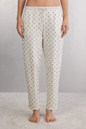 Romantische crèmekleurige pyjamabroek van zachte stof, voorzien van verspreide paarse bloemmotieven. Ze hebben een elastische tailleband met een koord.