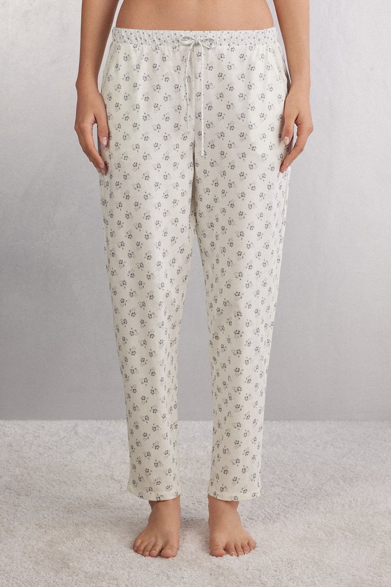 Romantische crèmekleurige pyjamabroek van zachte stof, voorzien van verspreide paarse bloemmotieven. Ze hebben een elastische tailleband met een koord.