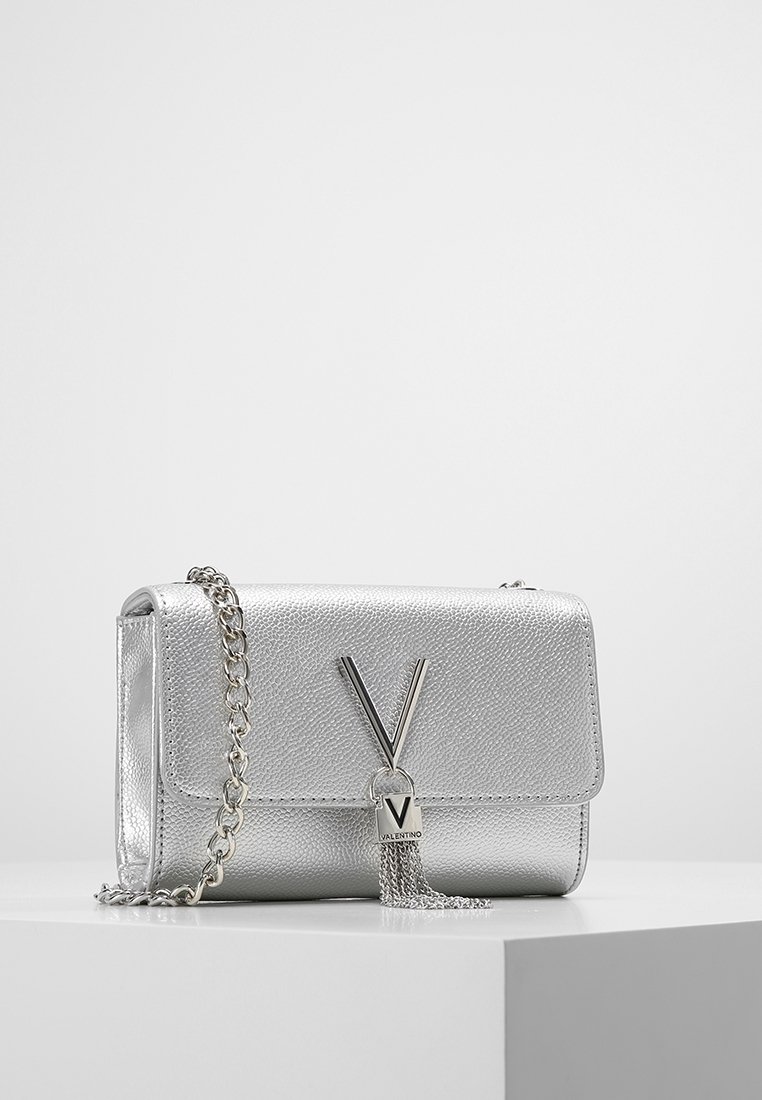 Silver metallic handbag with textured finish, flap closure, chain strap, and notable V-shaped hardware accent with tassel detail.