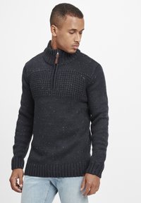 Stickad tröja i mörkblått med texturerad design och flerfärgade prickar. Har en dragkedja vid halsen samt ribbade ärmslut och nederkant.