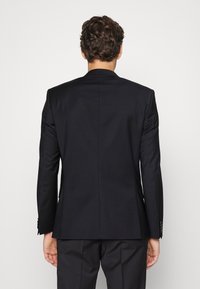 Zwarte op maat gemaakte blazer met een gestructureerd ontwerp, voorzien van een notch revers en enkele luchtopening, gemaakt van een gladde stof, die een strakke silhouet laat zien.