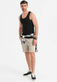 Zwarte katoenen tanktop, beige shorts, geruit shirt om de taille geknoopt, en zwarte sneakers met witte zolen. Casual outfit met een minimalistisch ontwerp.