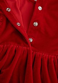 Czerwona sukienka z welwetu z marszczoną spódnicą, z metalowymi zatrzaskami z przodu oraz gładką podszewką w dopasowanym kolorze.