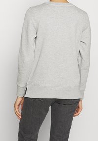 Grå sweatshirt med rund halsringning, långa ärmar och sidoflikar vid nederkanten. Tillverkad av mjukt tyg, minimal sömnadsdetalj vid ärmsluten.
