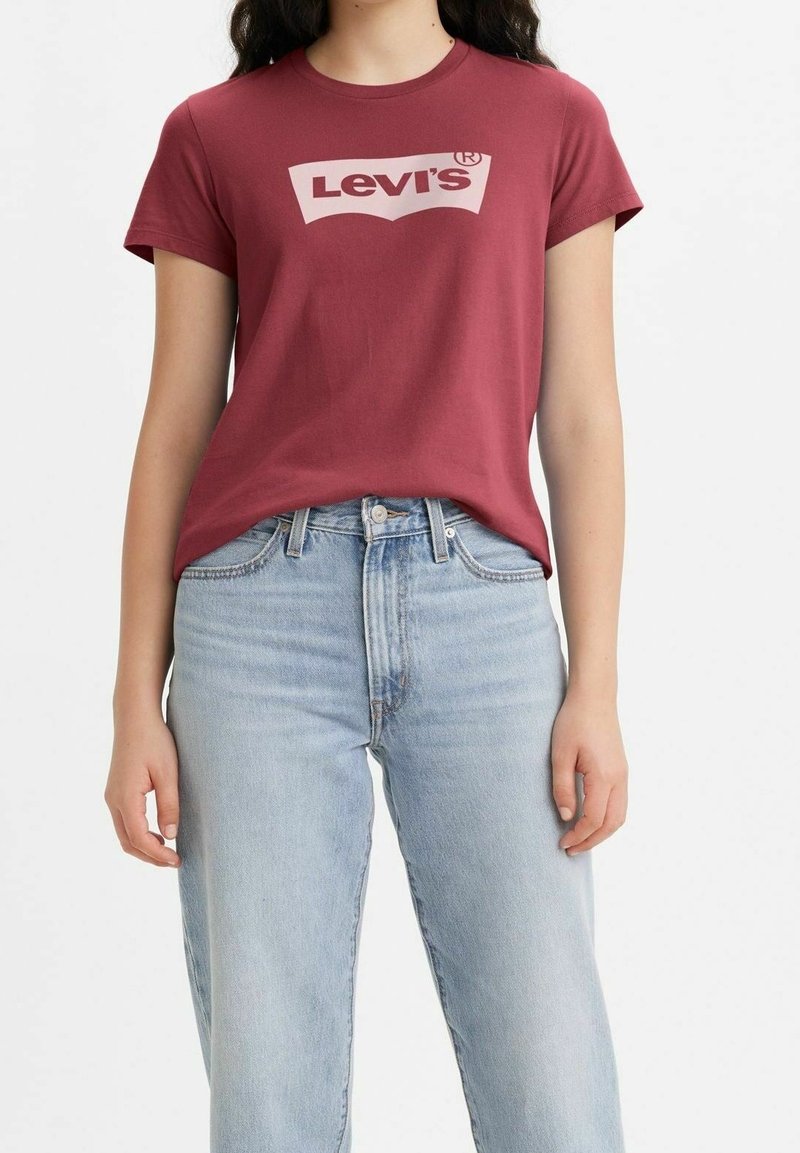 Maroon bomullströja med en stor ljusrosa Levi's-logotyp. Kombinerad med ljusblå högmidjade jeans. Kort ärm och rundad halsdesign.