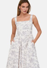 Ärmelloses Kleid in Hellbeige mit Blumenmuster, eckigem Ausschnitt, Taschen und gerafftem Rock. Aus weichem Stoff mit filigranen Mustern.