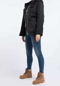 Musta vedenpitävä takki hupulla, raidallinen paita, siniset vartalonmyötäiset farkut ja vaaleanruskeat nilkkurit, joissa on nauhat ja kuvioidut pohjat.