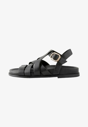 Black leather sandal with crisscross straps, flat sole, and an adjustable buckle accent. Smooth texture, minimalistic design.