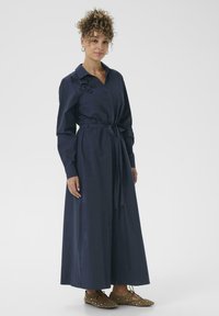 Robe maxi bleu marine à manches longues, taille ajustée, fermeture à boutons sur le devant, broderie florale sur l'épaule et ceinture assortie.