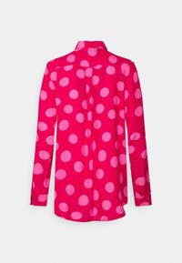 Långärmad skjorta i klar rosa med stora ljusrosa prickar. Har en krage och knappade ärmslut. Slät, flödande tyg.