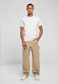 Witte katoenen t-shirt gecombineerd met beige cargo broek met zijzakken en messing accenten. Compleet met witte sneakers.