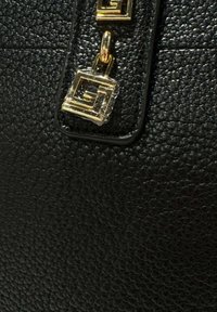Primo piano di pelle nera testurizzata con un pendente geometrico dorato attaccato da un'anello metallico.