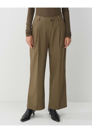 Femme portant un pantalon large taille haute olive avec fermeture à boutons et zip, haut marron à manches longues, et bottes noires à bout pointu.
