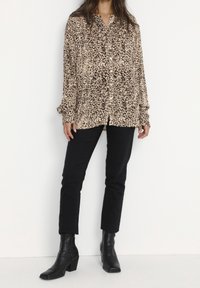 Leopard print long-sleeve blouse in beige and brown, featuring a button-down front and relaxed fit, paired with black slim-fit pants and black boots.